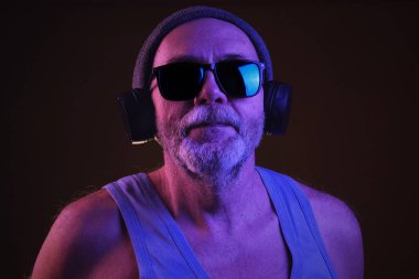 Gri şapkalı, kolsuz tişörtlü, siyah güneş gözlüklü, kulaklıklarıyla müzik dinleyen, şarkı söyleyen, kafasını sallayan, müzik eşliğinde dans eden sakallı yaşlı bir adam..