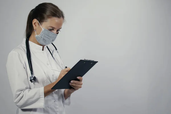 Female doctor in a white medical coat general practitioner physician with a phonendoscope making patients appointments schedule in notepad with pen