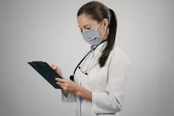 Lovely female doctor in a white medical coat general practitioner physician with a phonendoscope writing notes making patients appointments schedule in notepad