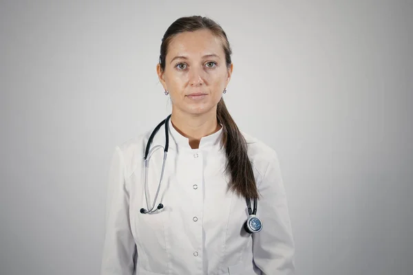 Koruyucu tıbbi maske takan genç kadın doktor portresi steteskopu takıyor ve doğrudan kameraya bakıyor. İzole edilmiş arkaplan