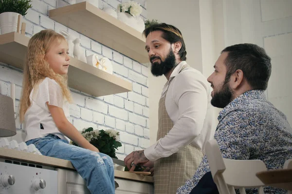 Evde kızı olan aynı cinsiyetten neşeli bir çift. Mutfakta yemek pişiren ve kızlarıyla konuşan eşcinsel erkek çift.