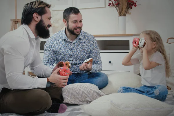 아파트 바닥에 앉아서 유약이 들어간 도넛을 가지고 귀여운 동성애 부부와 스톡 이미지