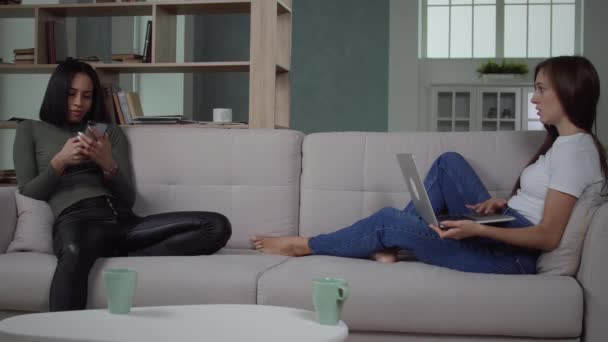 Κορίτσια που χρησιμοποιούν τη συσκευή κάθεται στον καναπέ. — Αρχείο Βίντεο