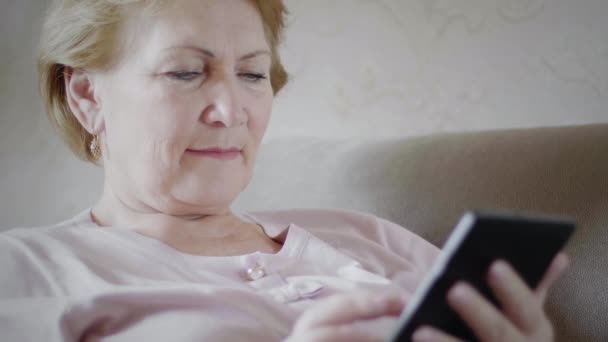 Femme âgée regardant la tablette numérique sur le canapé — Video