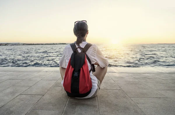 Una giovane donna si siede rilassata e guarda il tramonto sulla riva del mare . — Foto Stock