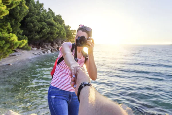 Вид от первого лица мужчины, который держит девушку за руку с фотокамерой на берегу моря . — стоковое фото