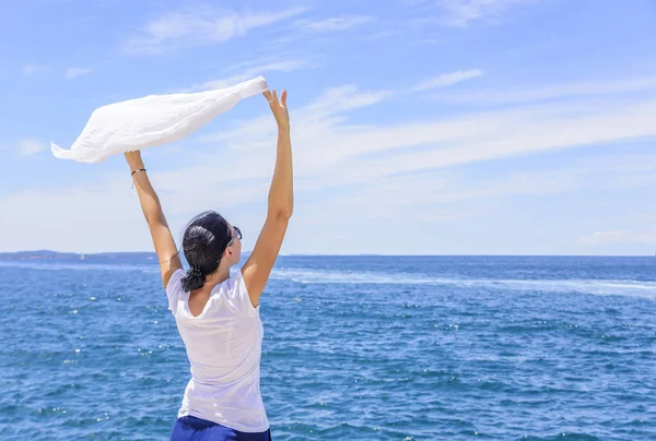 Kvinna som njuter av havsbrisen håller en siden näsduk vinkade av vinden mot havet. — Stockfoto