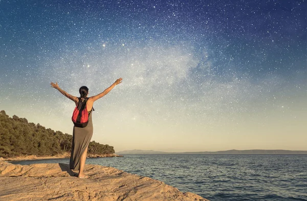 A young woman on the seashore raises her hands to the sky against the starry sky. — Stock Photo, Image