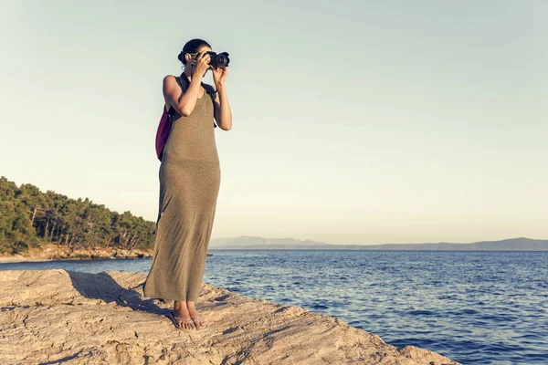Young woman photographer on a rocky seashore on evening. — Stock Photo, Image