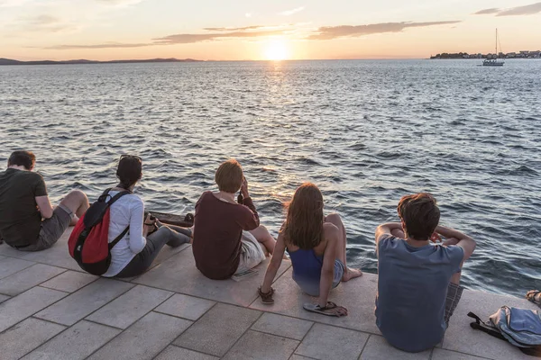 La gente siede sul bordo del terrapieno e guarda il tramonto del mare . — Foto Stock