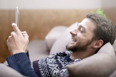 Tablet bilgisayar evde kanepede ellerinde olan genç adam.