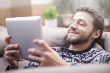 Tablet bilgisayar evde kanepede ellerinde olan genç adam.