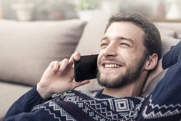 Vrolijke jongeman houden van mobiele telefoon en lachend thuis. — Stockfoto
