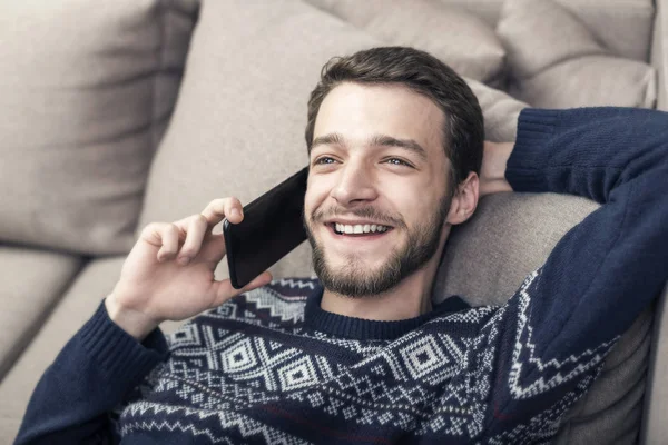 Joyeux jeune homme tenant un téléphone portable et souriant à la maison . — Photo