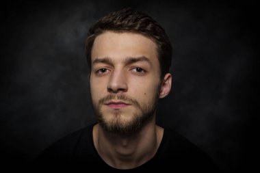 Karanlık bir arka plan üzerinde sakallı genç bir adam portresi.