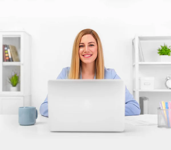 Attraente bionda in un abito blu in un ufficio luminoso che lavora su un computer portatile . — Foto Stock