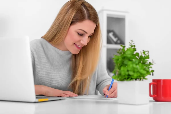 Jovem atraente de bom humor trabalha com documentos no escritório ou em casa. Escreve, preenche papéis na mesa com um laptop . — Fotografia de Stock