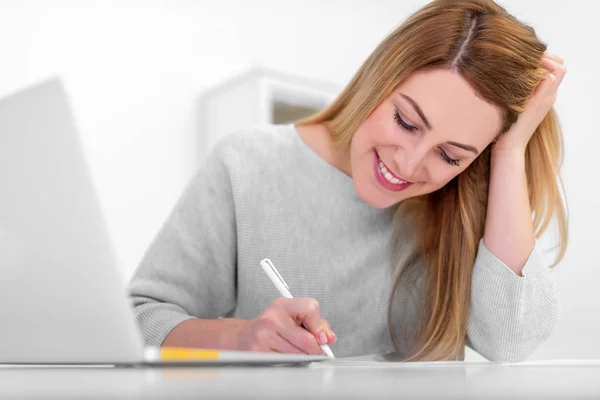 Attraktive junge Frau gut gelaunt arbeitet mit Dokumenten im Büro oder zu Hause. schreibt, füllt Papiere am Schreibtisch mit dem Laptop. — Stockfoto