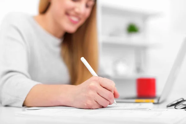 一个女人坐在办公室或教室的桌子旁写字。女孩使用笔记本电脑在工作场所填写文档. — 图库照片
