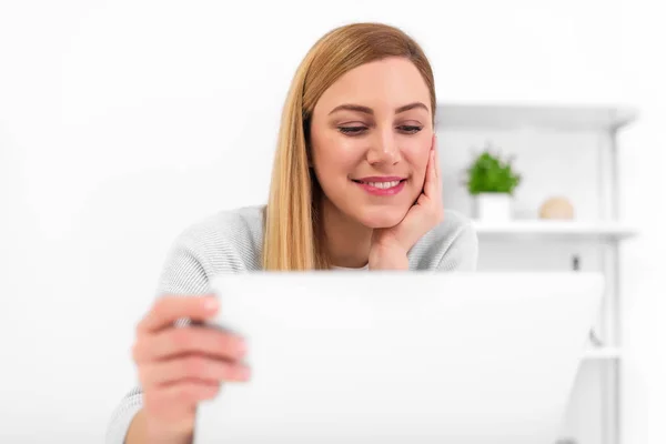 Loira em sua mesa em casa ou no escritório com um laptop e um copo vermelho . — Fotografia de Stock