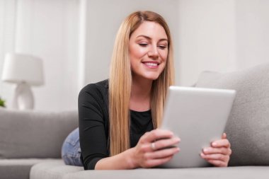 Çekici kadın evde kanepede yatan bir tablet PC'yi kullanma.