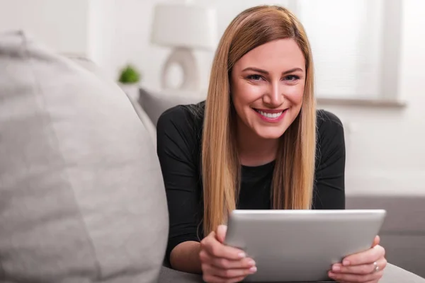 Femme attrayante utilisant un ordinateur tablette tout en étant couché sur le canapé à la maison . — Photo