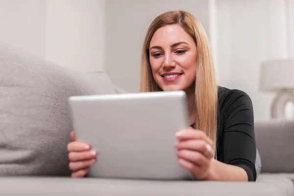 Femme attrayante utilisant un ordinateur tablette tout en étant couché sur le canapé à la maison . — Photo