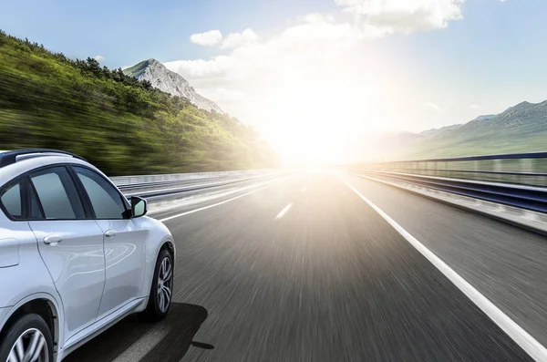 Un coche blanco corriendo a lo largo de una carretera de alta velocidad al sol . — Foto de Stock