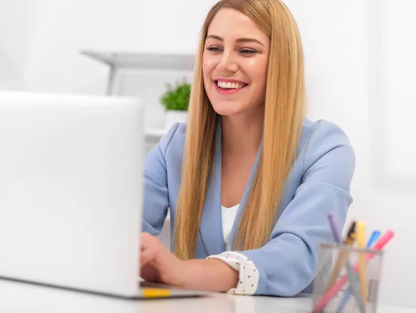 Mulher bonita olha para a tela do monitor do laptop enquanto está sentado na mesa do escritório . — Fotografia de Stock