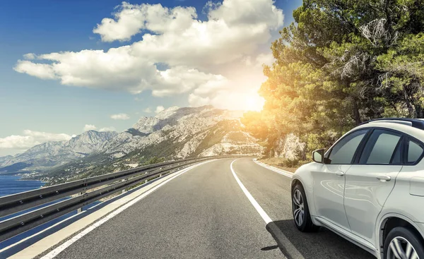 A white car rushing along a high-speed highway in the sun.