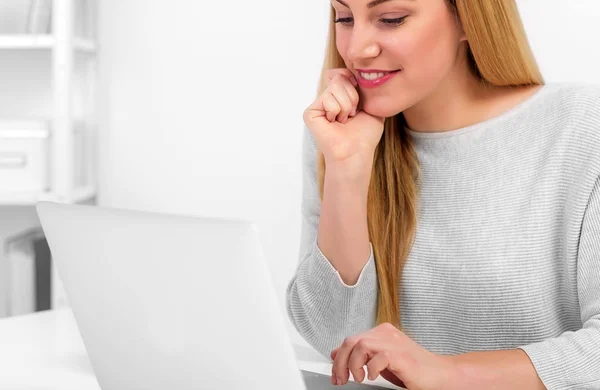 Attraktive blonde Frau schaut auf Laptop-Bildschirm, während sie am Schreibtisch im Büro oder zu Hause sitzt. — Stockfoto