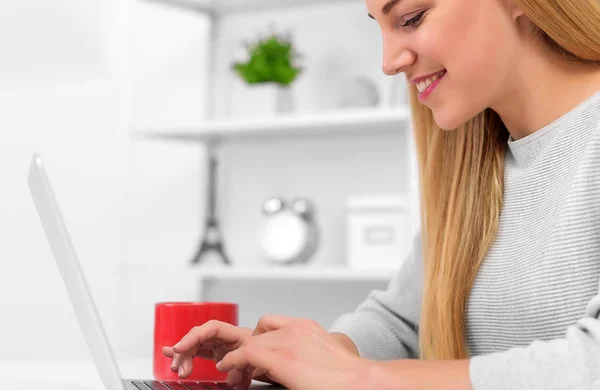 Blondine am Schreibtisch zu Hause oder im Büro mit Laptop und roter Tasse. — Stockfoto