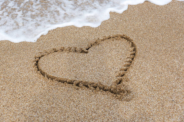 Drawing heart on the sand by the sea.