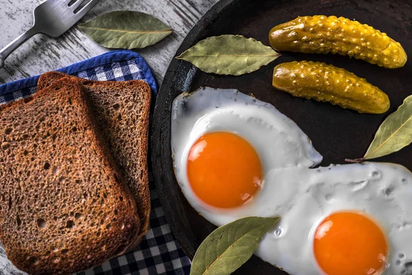 Spiegeleier in einer Pfanne. Roggen-Toast und eingelegte Gurken neben Spiegeleiern. — Stockfoto