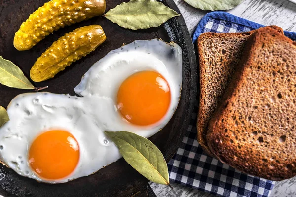 Spiegeleier in einer Pfanne. Roggen-Toast und eingelegte Gurken neben Spiegeleiern. — Stockfoto