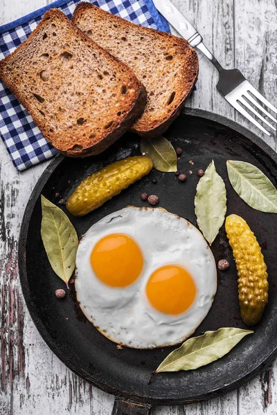 Spiegeleier in einer Pfanne. Roggen-Toast und eingelegte Gurken neben Spiegeleiern. — Stockfoto