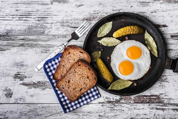 Αυγά τηγανιτά σε ένα τηγάνι. Τοστ σίκαλης και αγγουράκι τουρσί δίπλα τηγανητά αυγά. — Φωτογραφία Αρχείου