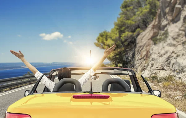 Jonge vrouw in een auto op de weg naar de zee tegen een achtergrond van prachtige bergen op een zonnige dag. — Stockfoto