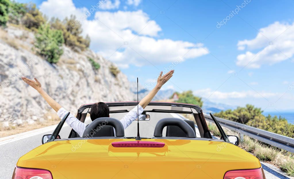 Young woman in a car on the road to the sea against a backdrop of beautiful mountains on a sunny day.