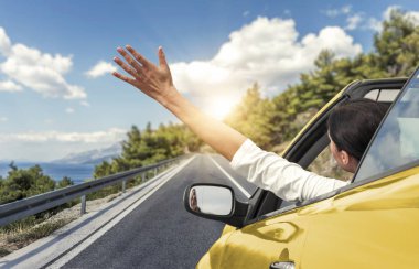 Genç bir kadın araba tarafından denize ve sarı bir Cabrio araba elini sallayarak. Deniz kıyısında tatil.