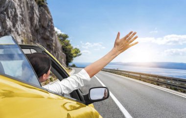 Genç bir kadın araba tarafından denize ve sarı bir Cabrio araba elini sallayarak. Deniz kıyısında tatil.