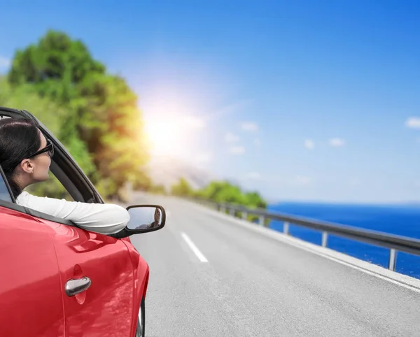 Mujer joven en un coche en el camino hacia el mar contra un telón de fondo de hermosos árboles en un día soleado . — Foto de Stock