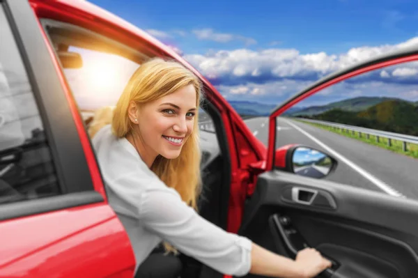 Vacker blond tjej som kör bil på motorvägen. Inbjudan till resor. Biluthyrning eller semester. — Stockfoto