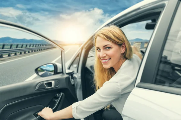 Menina loira bonita dirigindo um carro na estrada. Convite para viajar. Aluguer de automóveis ou férias . — Fotografia de Stock