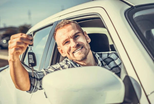 Ein männlicher Fahrer steht neben einem Auto mit einem Schlüssel in der Hand und lächelt. — Stockfoto