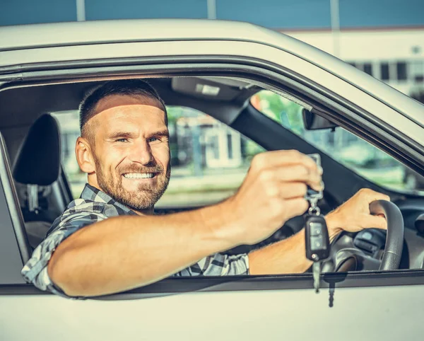 Un autista maschio sta vicino a una macchina con una chiave in mano e sorride . — Foto Stock