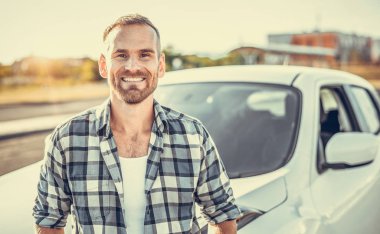 An attractive young man stands near a car.