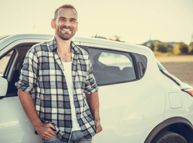 An attractive young man stands near a car.