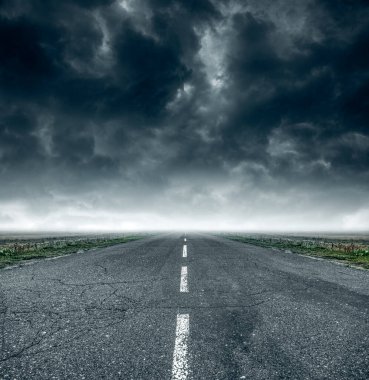 Bulutlu bir gökyüzüne karşı mesafeye giden yol.