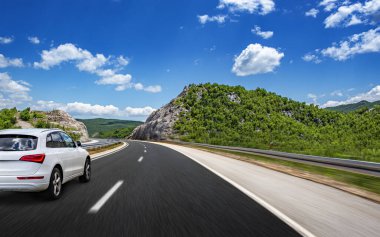 Araba, dağlar ve ormanlar arasında yolda ilerliyor..